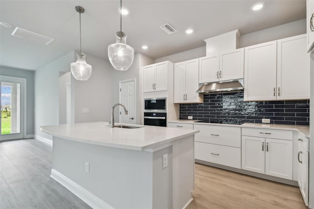 kitchen featuring pendant lighting, white cabinetry, an island with sink, and sink