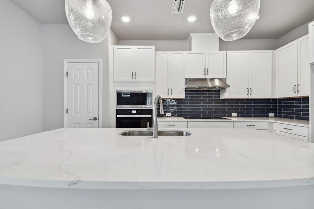 kitchen with white cabinetry, light stone countertops, sink, and pendant lighting