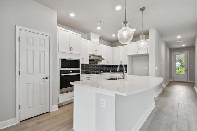 kitchen featuring appliances with stainless steel finishes, pendant lighting, sink, white cabinets, and a kitchen island with sink