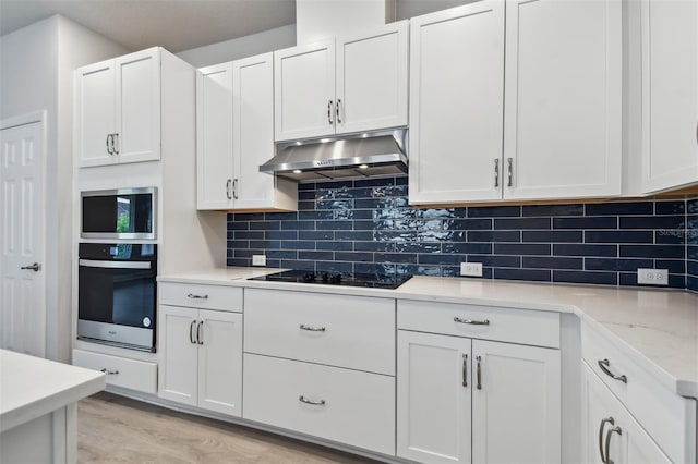 kitchen with appliances with stainless steel finishes, white cabinets, backsplash, light stone countertops, and light wood-type flooring