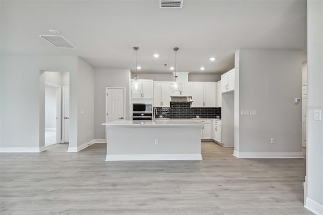 kitchen featuring pendant lighting, stainless steel appliances, a kitchen island with sink, decorative backsplash, and white cabinets