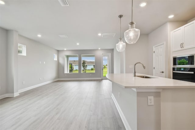 kitchen with pendant lighting, sink, a kitchen island with sink, oven, and light wood-type flooring