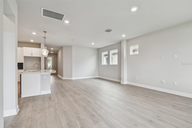 unfurnished living room featuring sink, light hardwood / wood-style floors, and a healthy amount of sunlight