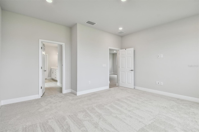 unfurnished bedroom with ensuite bath and light colored carpet