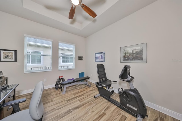 workout area featuring ceiling fan, a raised ceiling, and light hardwood / wood-style flooring