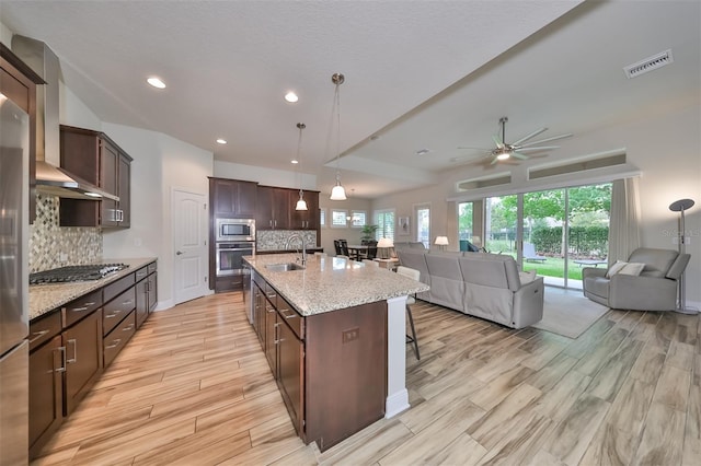 kitchen featuring sink, light stone counters, hanging light fixtures, appliances with stainless steel finishes, and a kitchen island with sink