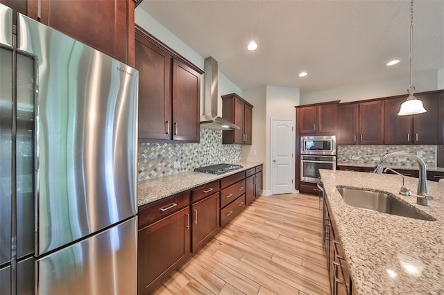 kitchen with wall chimney exhaust hood, sink, light stone counters, decorative light fixtures, and stainless steel appliances