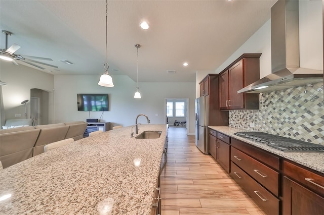 kitchen with sink, stainless steel appliances, light stone countertops, decorative light fixtures, and wall chimney exhaust hood