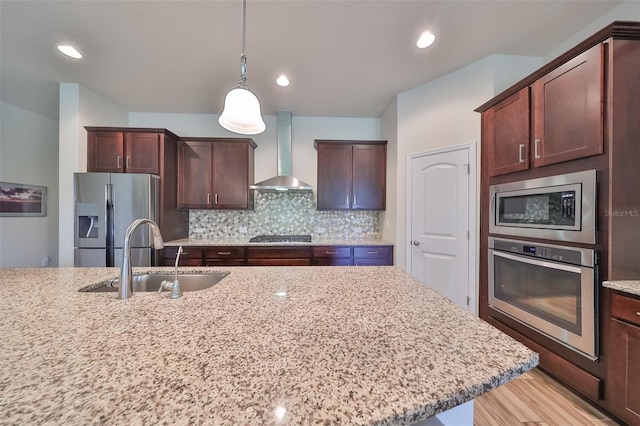 kitchen featuring light stone counters, wall chimney exhaust hood, stainless steel appliances, and sink