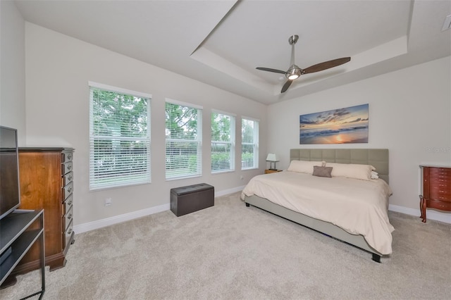 bedroom featuring a raised ceiling, light colored carpet, and ceiling fan