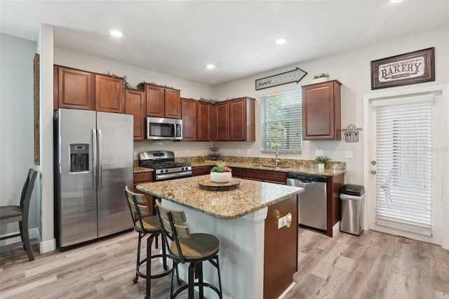 kitchen with a breakfast bar, a center island, stainless steel appliances, light stone countertops, and light hardwood / wood-style flooring