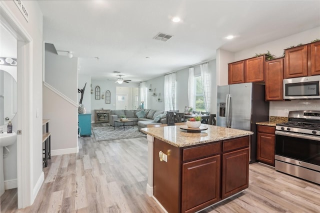 kitchen with appliances with stainless steel finishes, a kitchen island, ceiling fan, light stone countertops, and light hardwood / wood-style floors