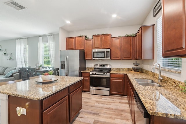 kitchen featuring stainless steel appliances, a center island, sink, and light stone counters