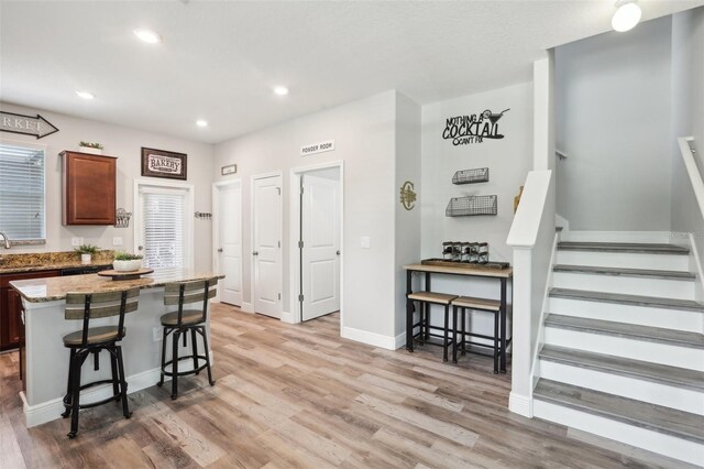 kitchen featuring a breakfast bar, light stone countertops, a center island, light hardwood / wood-style floors, and sink