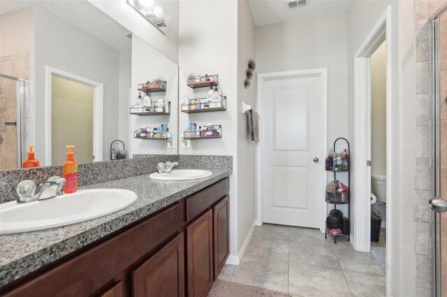 bathroom with walk in shower, toilet, dual bowl vanity, and tile patterned floors