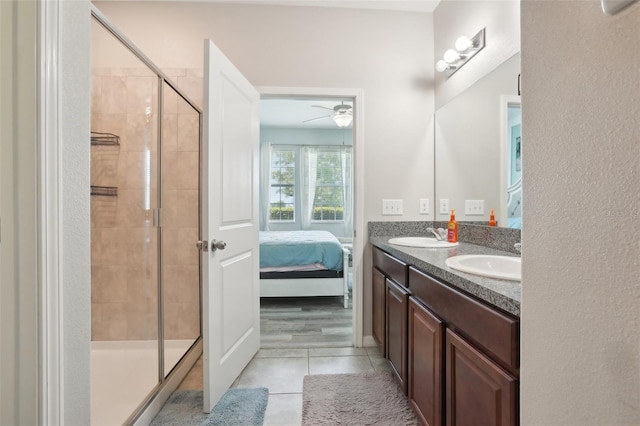 bathroom featuring a shower with shower door, ceiling fan, dual bowl vanity, and tile patterned flooring