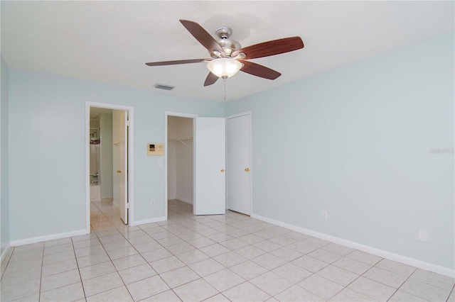 unfurnished bedroom featuring light tile patterned floors, a spacious closet, ceiling fan, and a closet