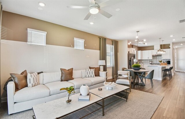 living room featuring ceiling fan with notable chandelier, a wealth of natural light, and light wood-type flooring