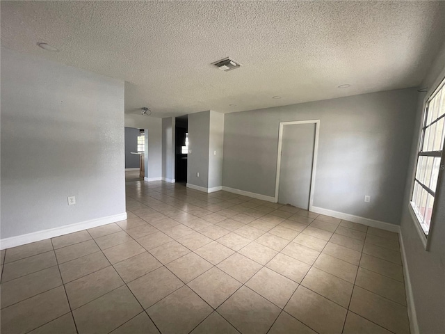 tiled spare room with a textured ceiling and a healthy amount of sunlight