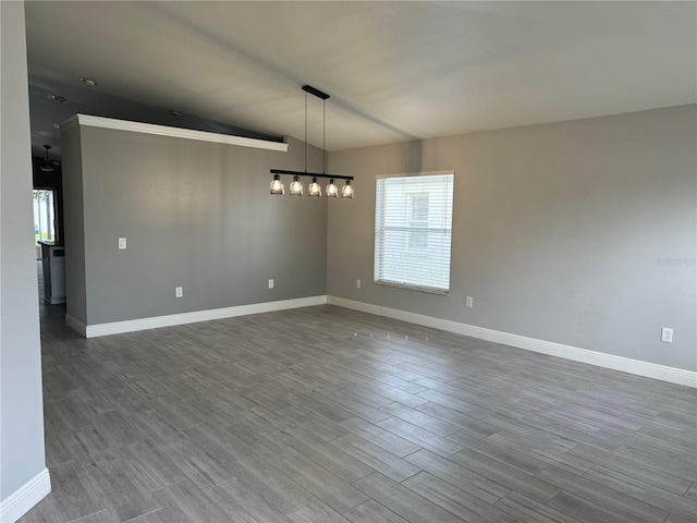 empty room with a notable chandelier, vaulted ceiling, and hardwood / wood-style floors