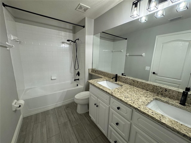 full bathroom with a textured ceiling, toilet, double vanity, tiled shower / bath combo, and hardwood / wood-style floors