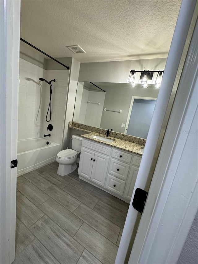 full bathroom with a textured ceiling, toilet, tile patterned floors, tiled shower / bath combo, and vanity