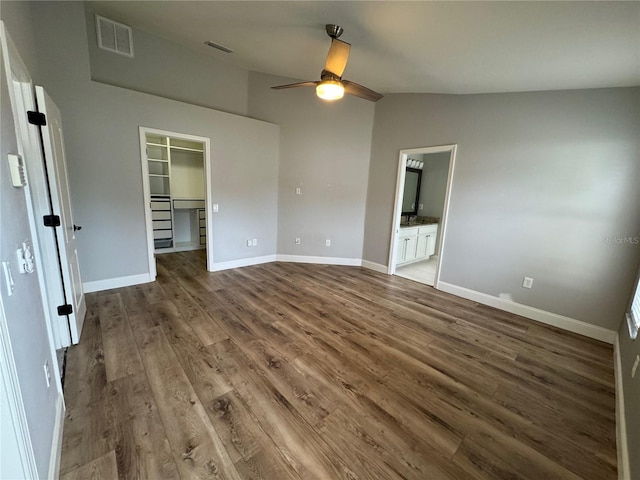 unfurnished bedroom featuring connected bathroom, lofted ceiling, a spacious closet, a closet, and hardwood / wood-style floors