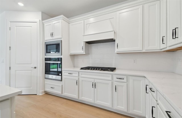 kitchen with light stone countertops, appliances with stainless steel finishes, tasteful backsplash, light hardwood / wood-style floors, and white cabinetry