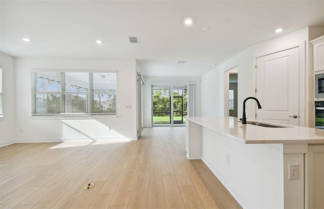 kitchen with appliances with stainless steel finishes, sink, a center island with sink, light hardwood / wood-style flooring, and white cabinets