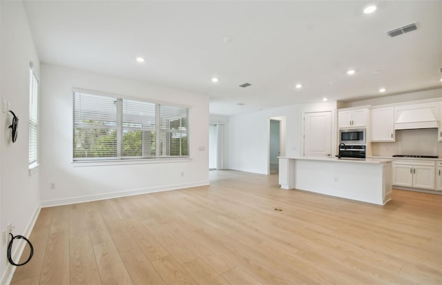 kitchen featuring white cabinetry, a center island with sink, appliances with stainless steel finishes, custom range hood, and light wood-type flooring