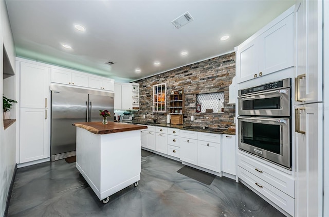 kitchen with wood counters, tasteful backsplash, a center island, stainless steel appliances, and white cabinets