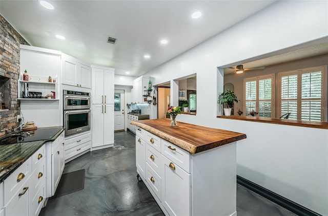 kitchen featuring a kitchen island, butcher block countertops, white cabinetry, ceiling fan, and stainless steel double oven