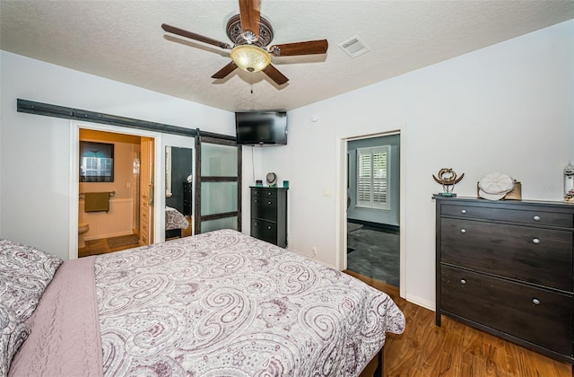 bedroom featuring ensuite bath, wood-type flooring, a barn door, and a textured ceiling