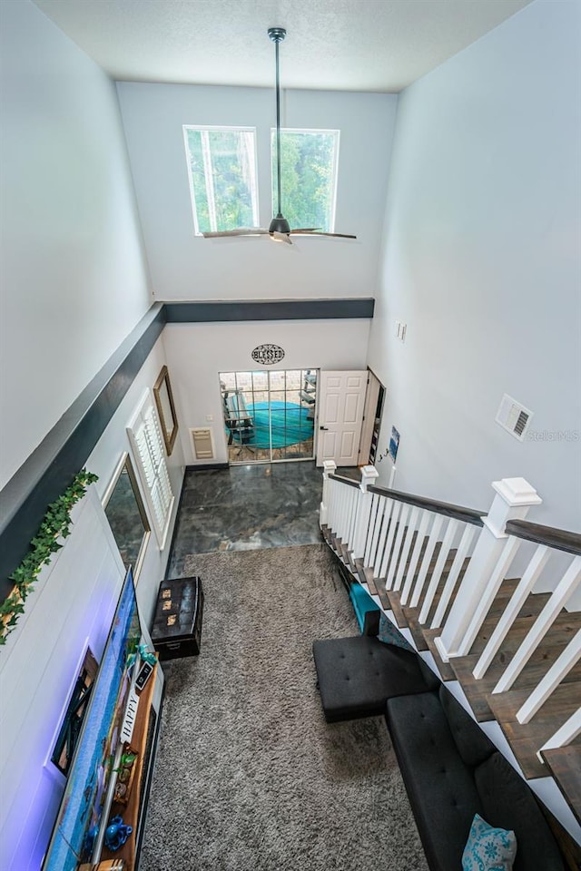 stairs with a towering ceiling, ceiling fan, and carpet