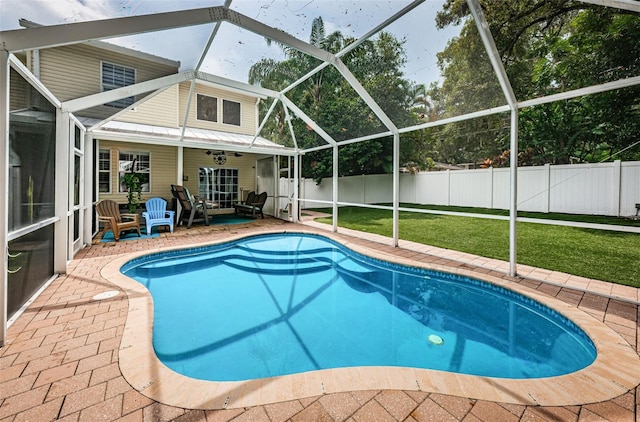 view of swimming pool with a patio area, a lawn, ceiling fan, and glass enclosure