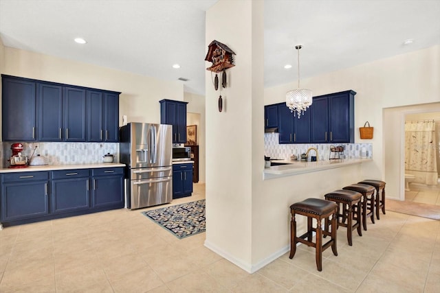 kitchen featuring a kitchen breakfast bar, blue cabinets, appliances with stainless steel finishes, kitchen peninsula, and a chandelier