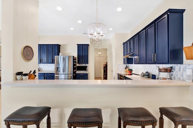 kitchen with tasteful backsplash, kitchen peninsula, hanging light fixtures, blue cabinets, and appliances with stainless steel finishes