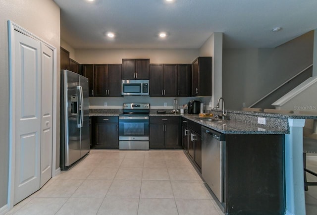 kitchen featuring appliances with stainless steel finishes, dark stone counters, light tile patterned floors, sink, and kitchen peninsula