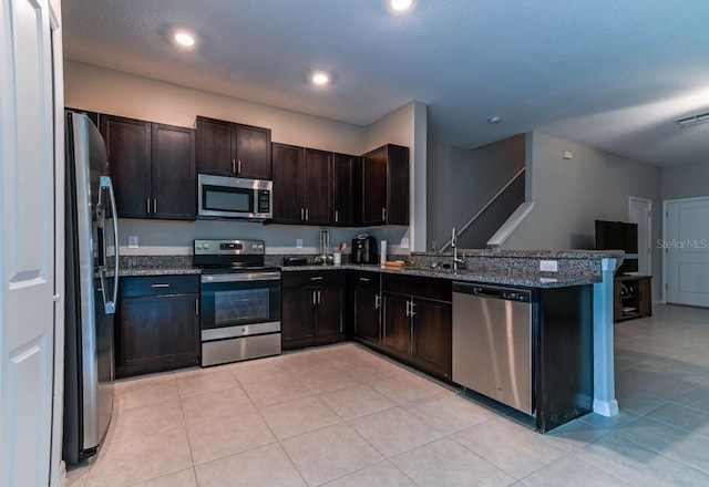 kitchen featuring light tile patterned floors, appliances with stainless steel finishes, kitchen peninsula, and dark stone counters