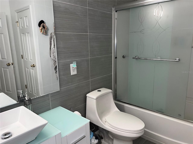 full bathroom featuring bath / shower combo with glass door, sink, tile walls, and toilet