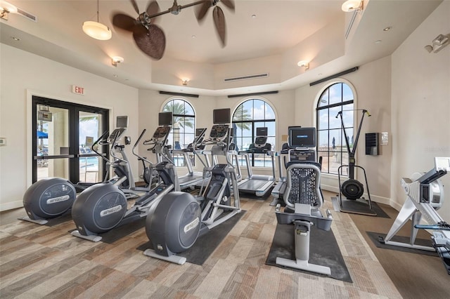 gym with a towering ceiling, ceiling fan, and a tray ceiling