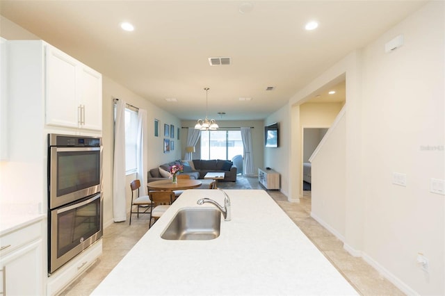 kitchen with stainless steel double oven, sink, decorative light fixtures, a chandelier, and white cabinetry