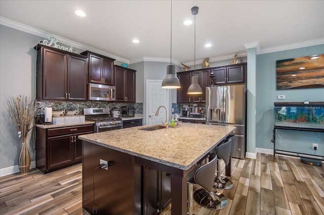 kitchen with appliances with stainless steel finishes, light hardwood / wood-style floors, sink, a center island with sink, and a breakfast bar