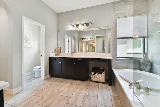 bathroom with tile patterned floors, vanity, a relaxing tiled tub, and toilet