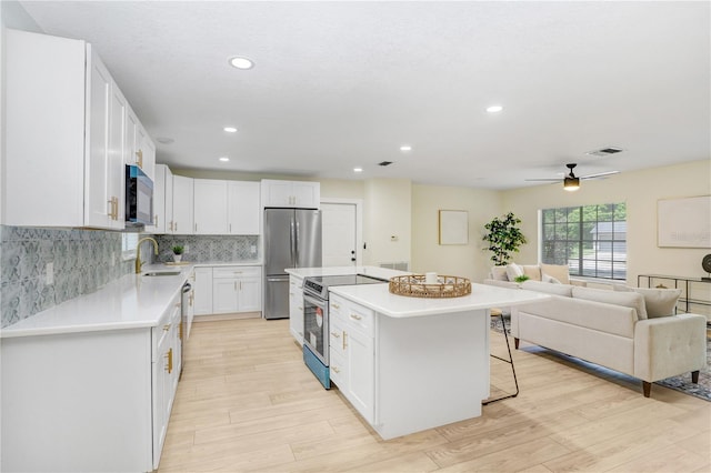 kitchen featuring stainless steel appliances, a kitchen island, light countertops, and white cabinets