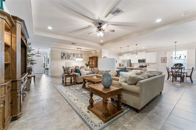 living room with a raised ceiling, light tile patterned flooring, and ceiling fan with notable chandelier