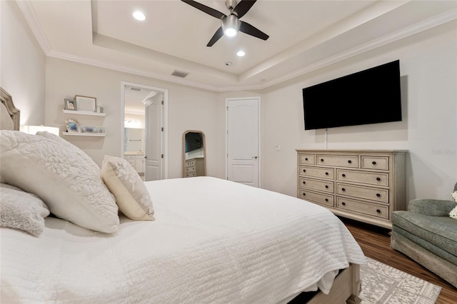 bedroom with a raised ceiling, crown molding, ensuite bath, ceiling fan, and dark wood-type flooring