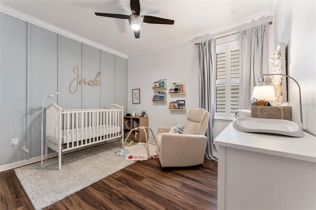 bedroom featuring a crib, dark hardwood / wood-style flooring, ornamental molding, and ceiling fan