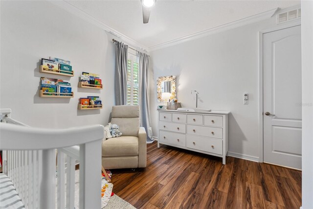 bedroom with ceiling fan, a nursery area, ornamental molding, and dark hardwood / wood-style floors