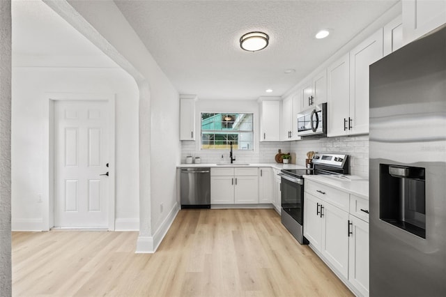 kitchen with sink, stainless steel appliances, white cabinetry, and light hardwood / wood-style floors